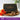 Booja-Booja chocolate box with chocolates on a wooden board with orange roses and a plant in the background.